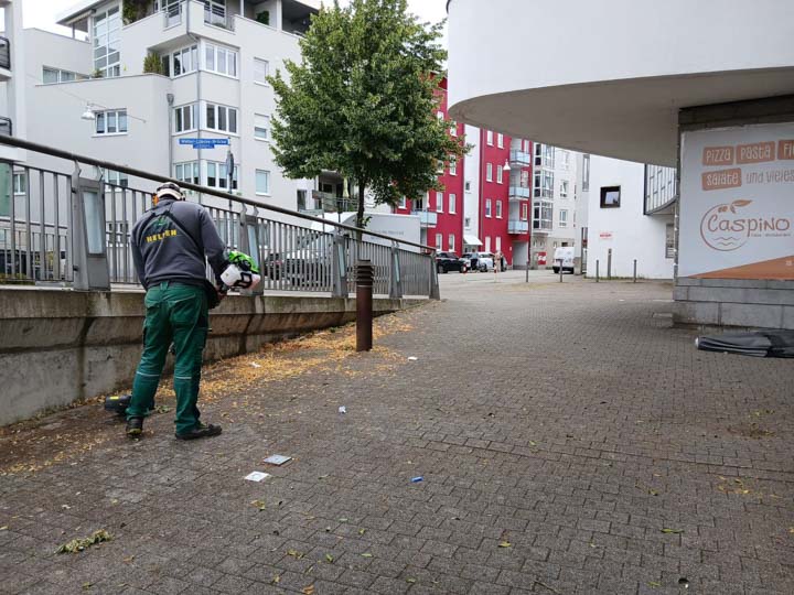 Mitarbeiter bei Laub- und Pflegearbeiten an einer gepflasterten Gewerbefläche
