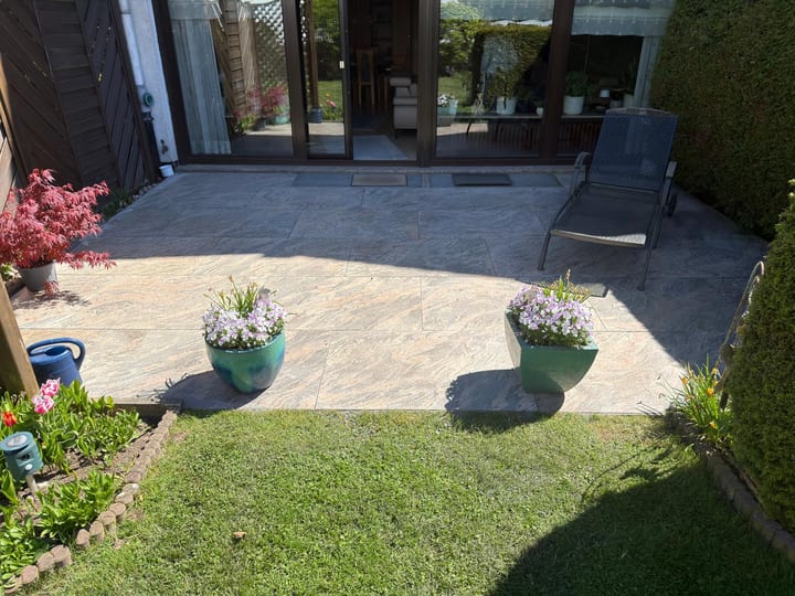 Terrasse mit großformatigen Natursteinplatten vor einer Glasfront im Garten